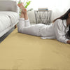 Person lying on a camel beige rabbit fur carpet in a room with a couch and plant