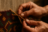 : A close-up of a skilled artisan’s hands weaving a rug, strong and precise, with vibrant natural wool threads, showing the intricate knots and sturdy craftsmanship, earthy tones, depth of field, high realism.