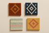 A flat lay of four small rug swatches, each with a distinct seasonal palette — autumn tones with rust and ochre, winter blues and ivory, spring pastels, summer gold and coral — arranged artistically on a neutral background, soft natural light highlighting textures, modern and visually balanced presentation.