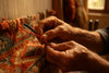 A high-quality photo of an artisan in mid-process — tufting, trimming, or knotting a rug. Close-up on hands and tools, showing texture and detail of the yarn. Warm, natural light for authenticity.