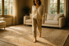 : A luxurious, hand-knotted rug in a cozy living room, sunlight streaming through large windows, a person walking barefoot on the rug with a soft smile, the texture visibly plush and inviting, warm neutral tones, high detail, cinematic lighting.