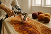 A skilled artisan hand-tufting a luxurious rug in a bright, elegant studio — close-up of hands guiding the tufting gun with precision, soft wool yarns in autumnal tones on the side, detailed texture showing carved patterns and depth — warm lighting, minimal and refined background, cinematic composition.