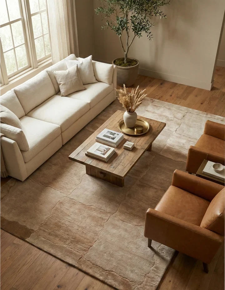 Hand-tufted rug in a warm neutral tone with a subtle abstract pattern, styled beneath a coffee table in a modern living room.