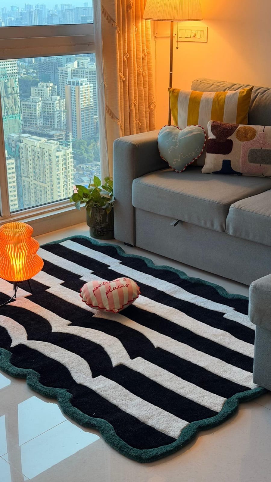Living room with a black and white striped rug, colorful pillows, and a cityscape view.