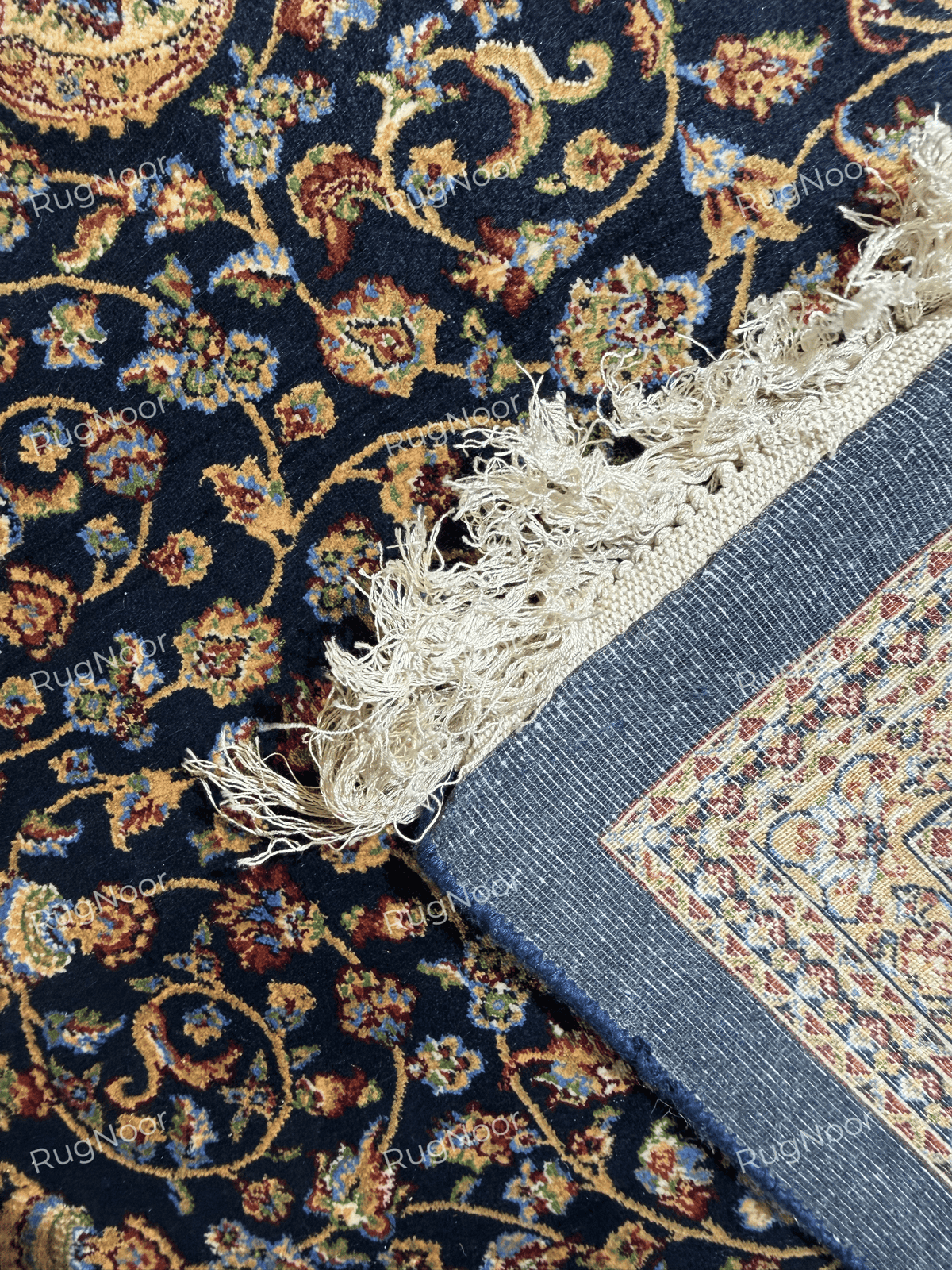 Close-up of the Shabafruz rug’s blue backing, woven edge, ivory fringe, and navy floral pile.