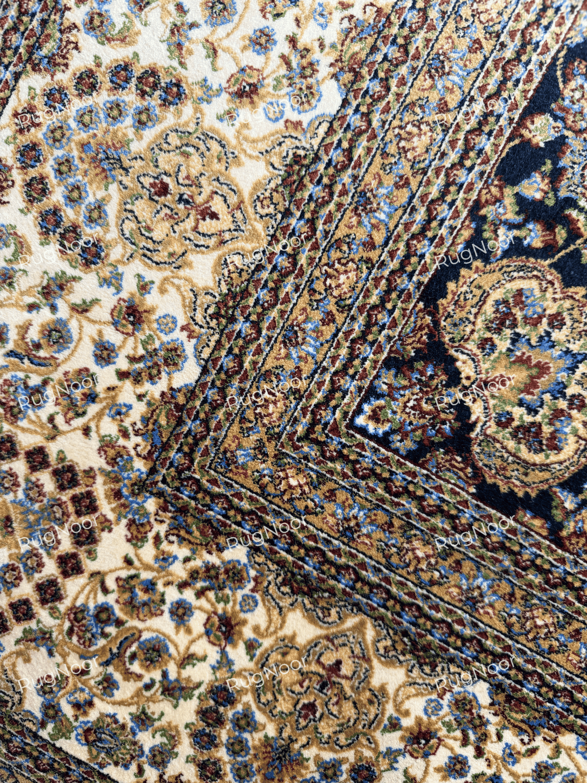 Close-up of the Shabafruz rug’s ivory floral border meeting the dark navy inner border at a corner.