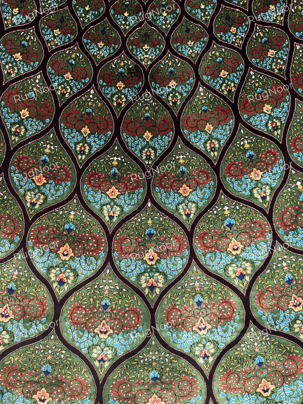 Detailed view of the Tawus carpet's repeating teardrop motifs filled with colourful floral designs.