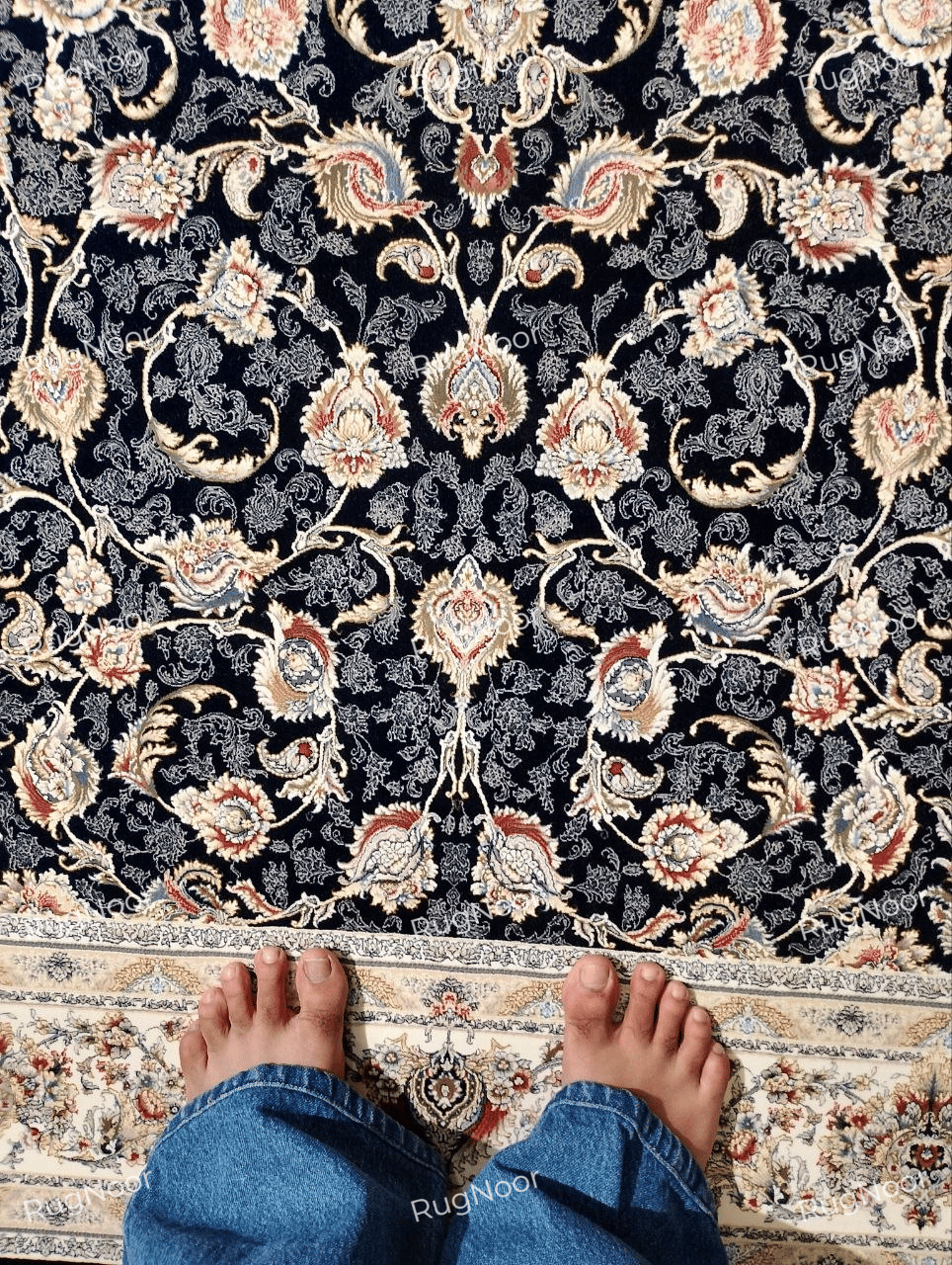 Close-up of the Zarniva traditional floral carpet showing intricate ivory scrolling vines, symmetrical floral motifs and rust, gold and pale blue accents on a navy background.