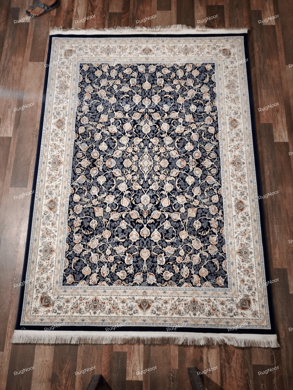 Zarniva 5x7 traditional floral carpet with a navy blue centre, intricate ivory floral motifs, a multicolour ornamental border and ivory fringe.
Copy alt text