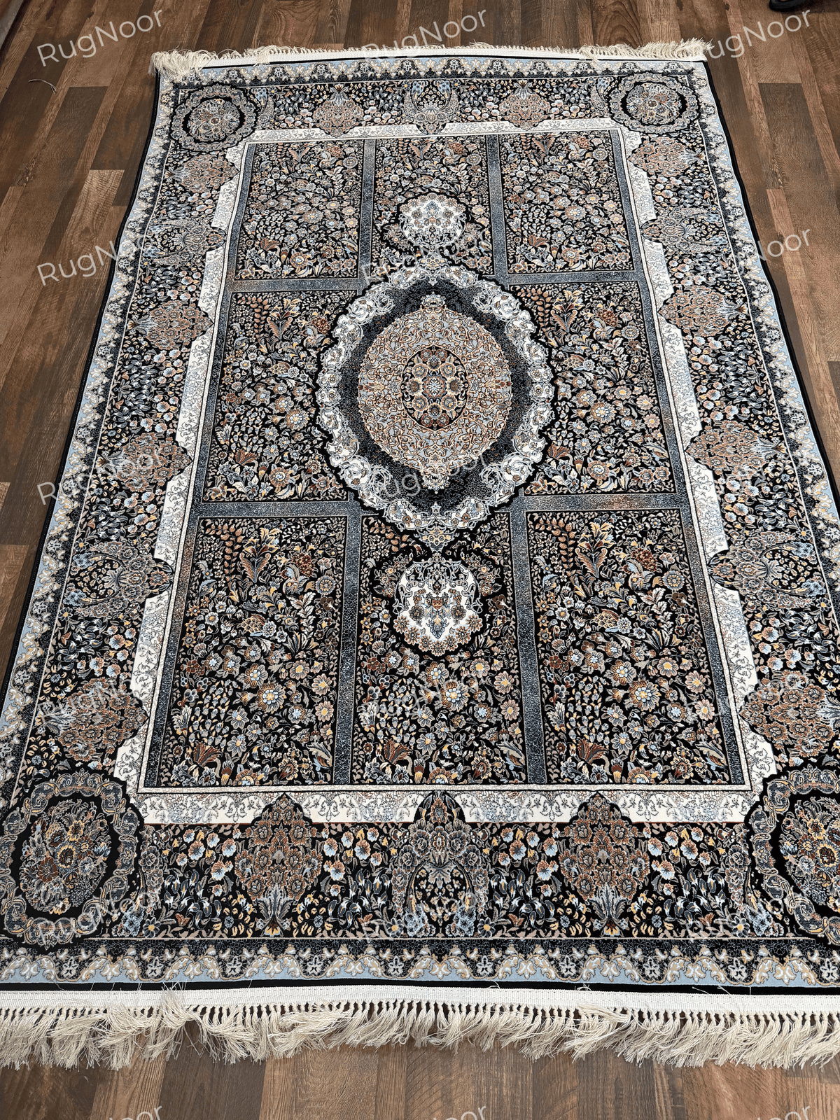 Full view of a black Irani carpet with floral panels, oval medallion, ornate borders, and fringe by RugNoor