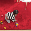 Child playing on a maroon rabbit fur carpet with toys