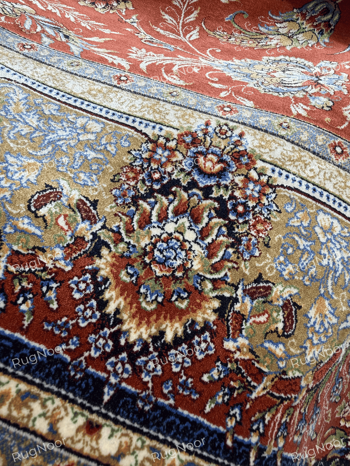 Close-up of Atashgul's pale blue and gold floral border beside the terracotta field.