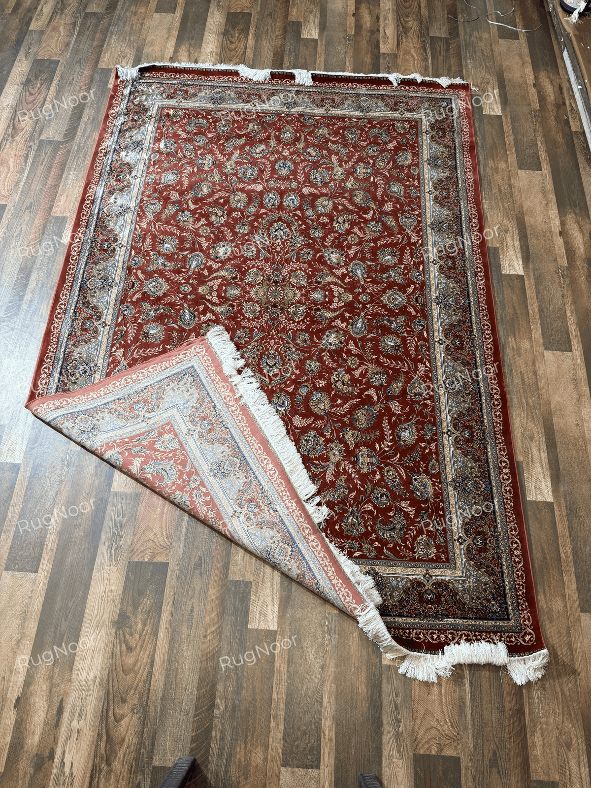 Atashgul rug lifted by its fringed edge, showing the underside and layered border.