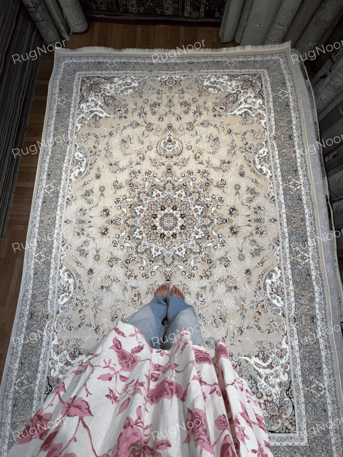Full view of the beige Urkeed carpet with an ornate floral centre and layered grey border in a showroom, RugNoor.
