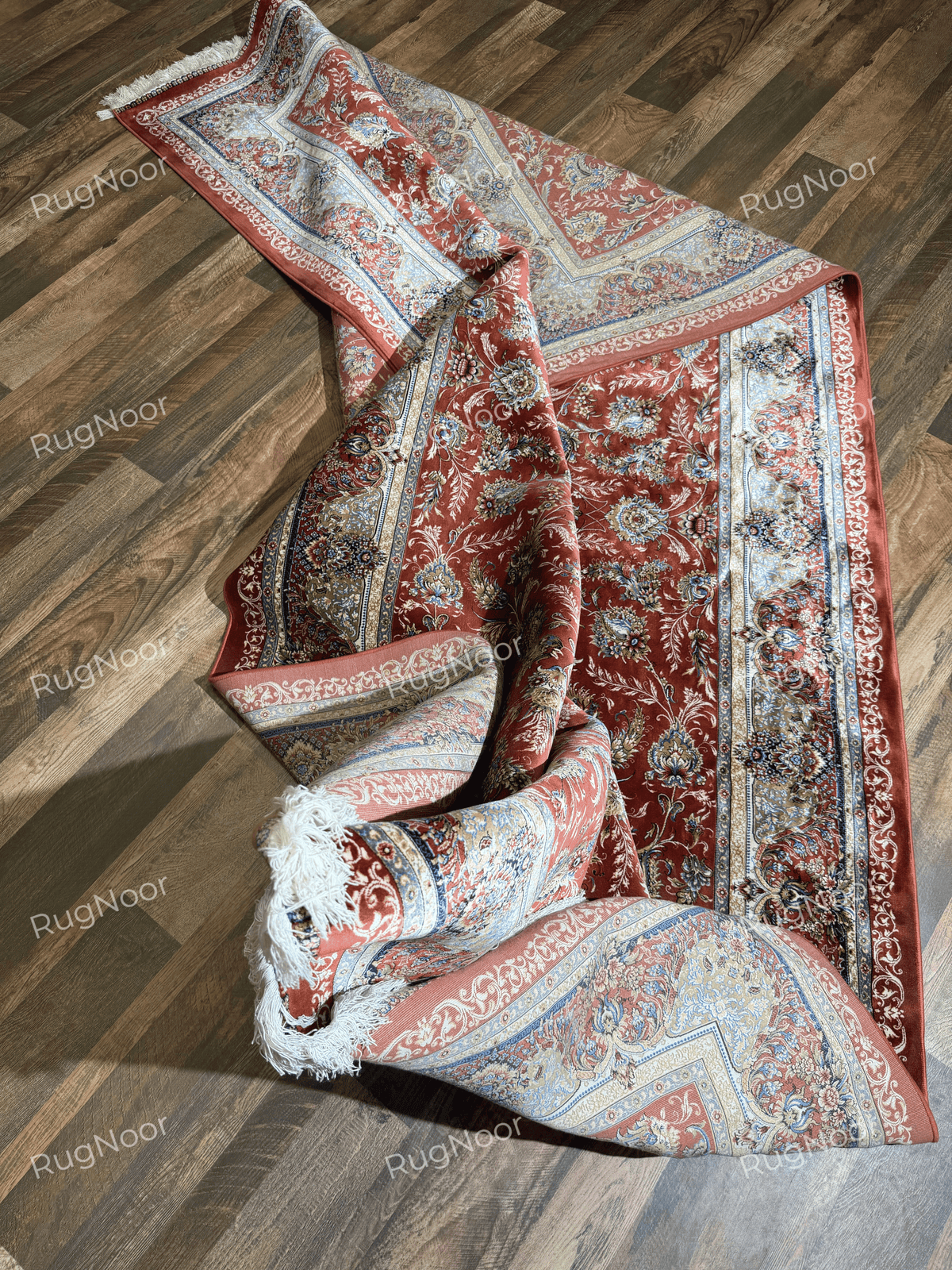 Atashgul rug loosely rolled and folded on the floor, showing its patterned surface, border, and fringe.