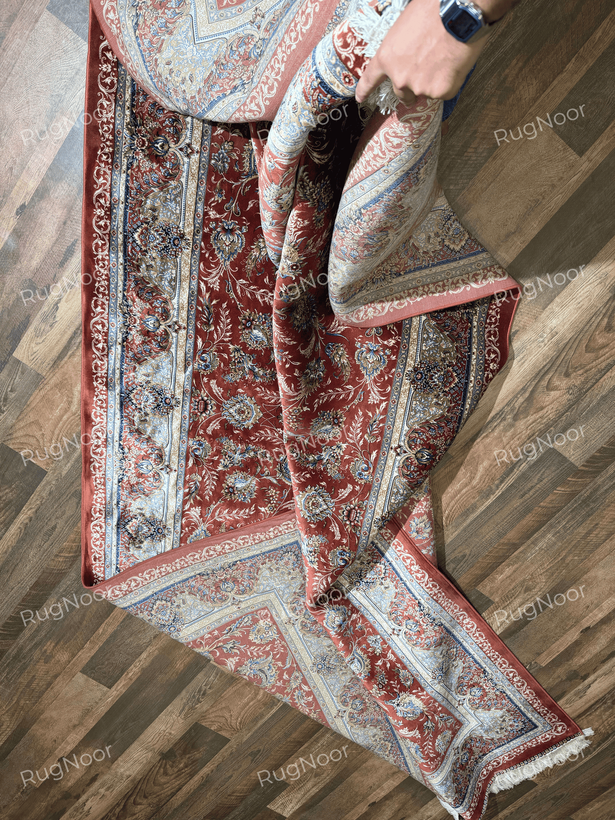 Atashgul rug loosely folded across itself, exposing sections of the terracotta pattern and pale border.