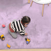 Child playing on a light purple rabbit fur carpet with toys