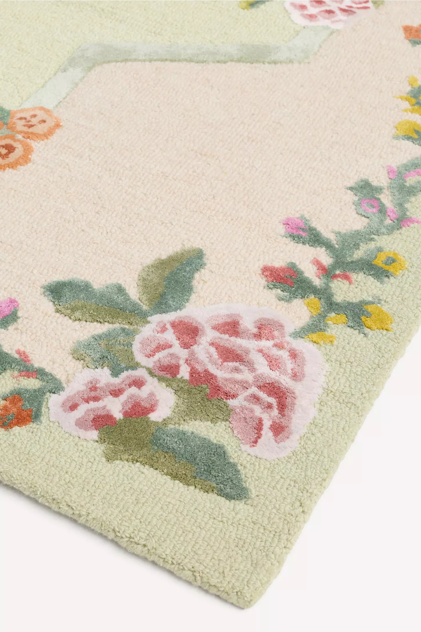 Close-up of a textured area rug with a pale sage green base, featuring a raised floral border with pink roses, green leaves, and small yellow and orange blossoms.