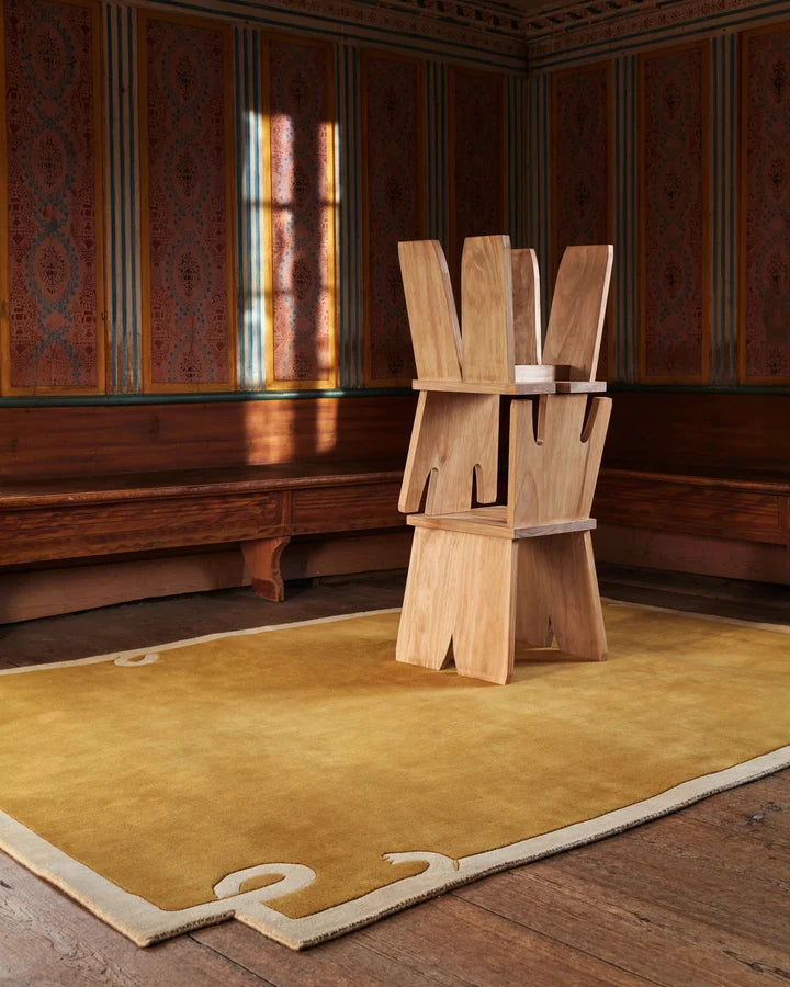 Mustard hand tufted wool rug with sculpted border styled in a contemporary interior with natural wood furniture.