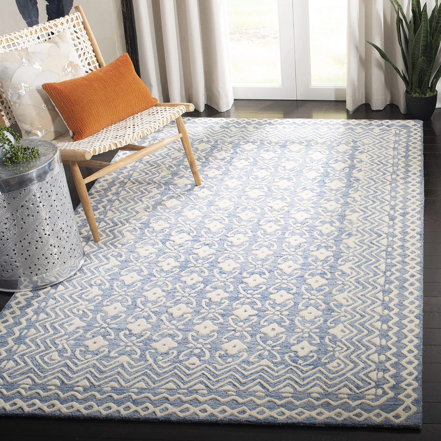 Hand tufted powder blue and ivory wool rug with carved floral motifs and geometric borders styled in a bright modern living room with a woven accent chair.