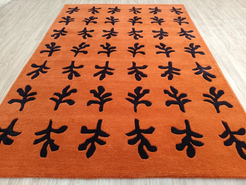 Angled view of the Brio hand tufted wool rug highlighting its bold black botanical motifs on a rich terracotta background.