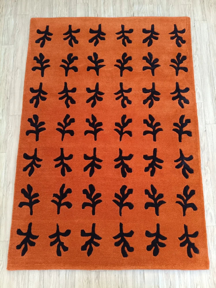Hand tufted terracotta wool rug featuring repeating black abstract botanical motifs arranged in a clean minimalist grid pattern.