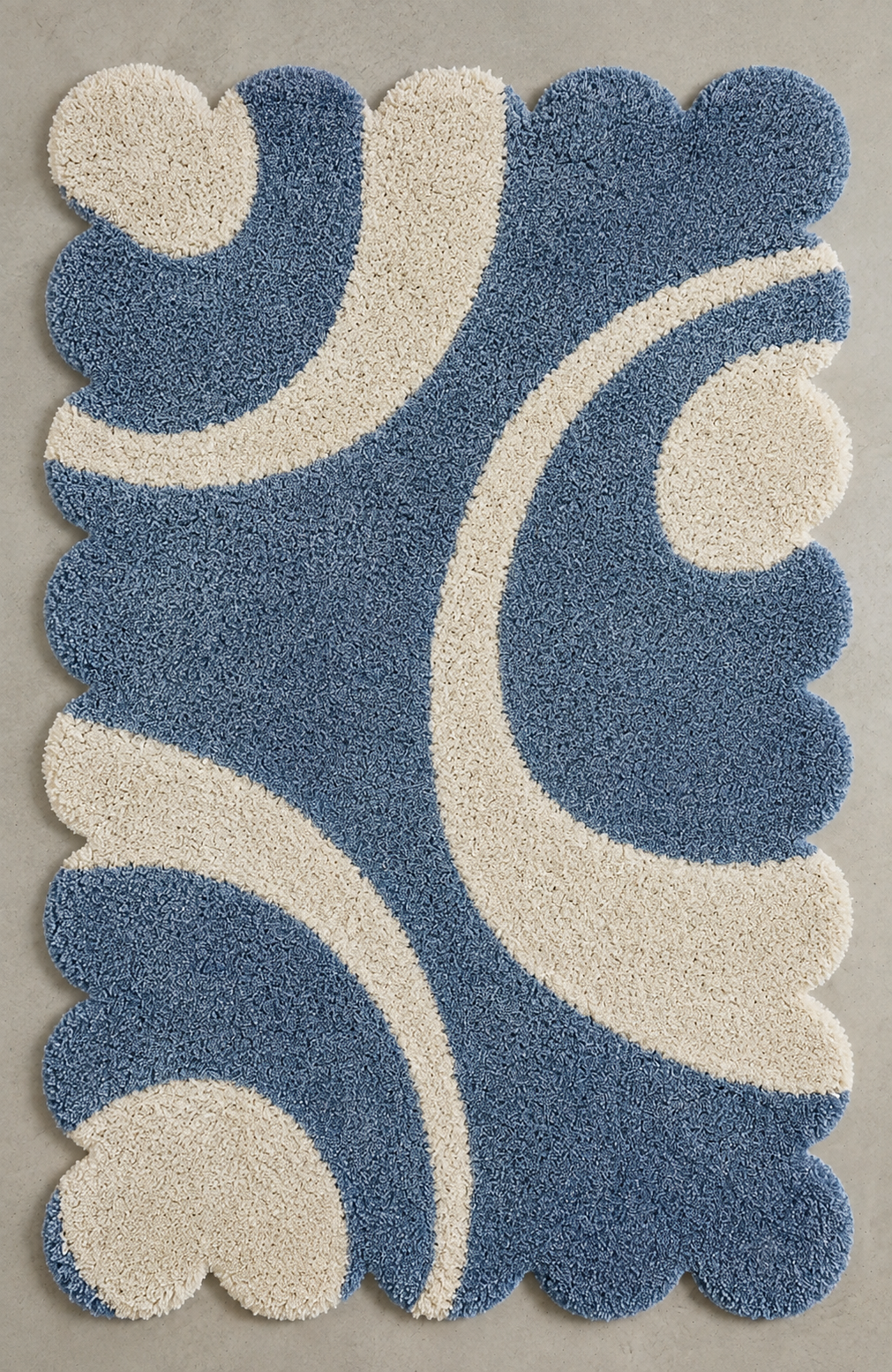 A rectangular shag rug with a scalloped edge, featuring an abstract wavy pattern in medium blue and cream on a light gray background.