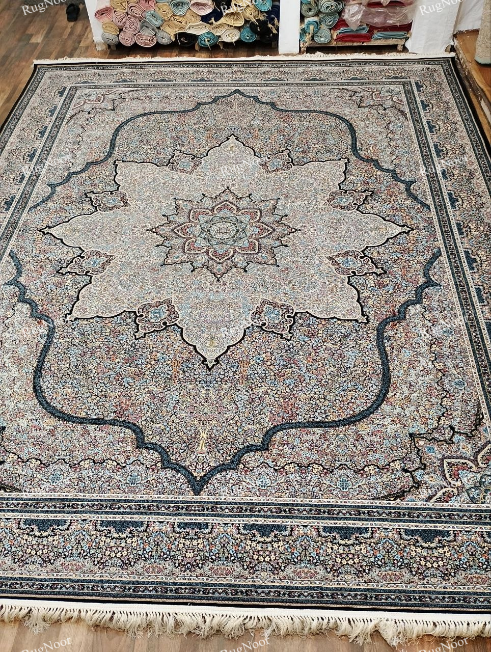 Full view of the Azrinah 10x14 ivory medallion carpet featuring a large ornate central medallion, intricate multicolour motifs, layered borders, and ivory fringe.
