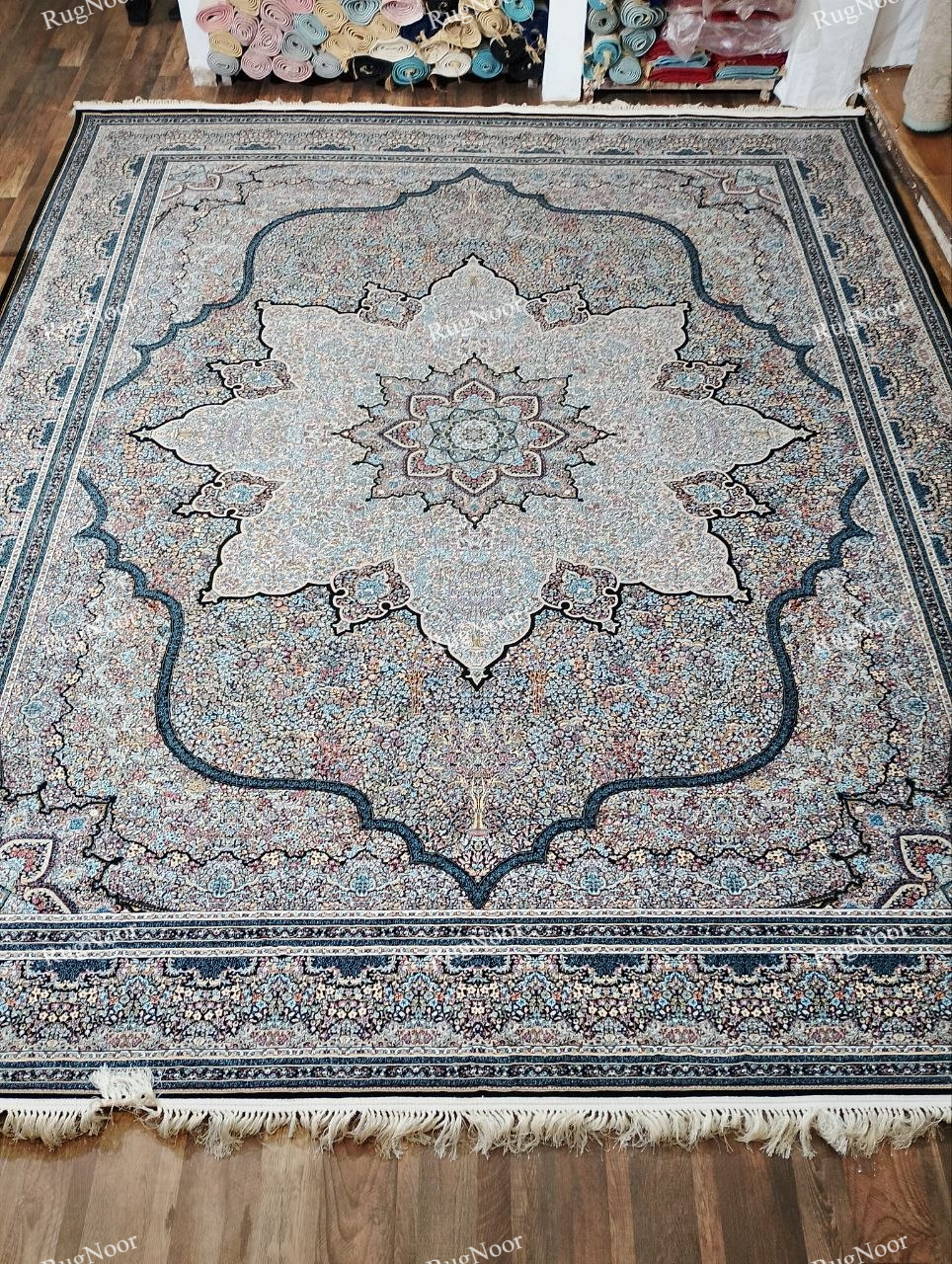 Full view of the Azrinah 10x14 ivory medallion carpet featuring a large ornate central medallion, intricate multicolour motifs, layered borders, and ivory fringe.