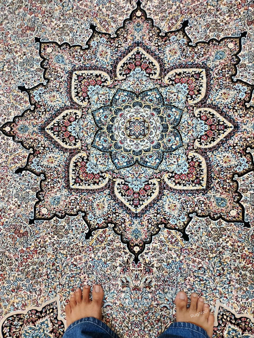Close-up of the Azrinah ivory medallion carpet showing detailed ornamental motifs in dusty blue, blush pink, rust, muted gold, and dark navy-black.