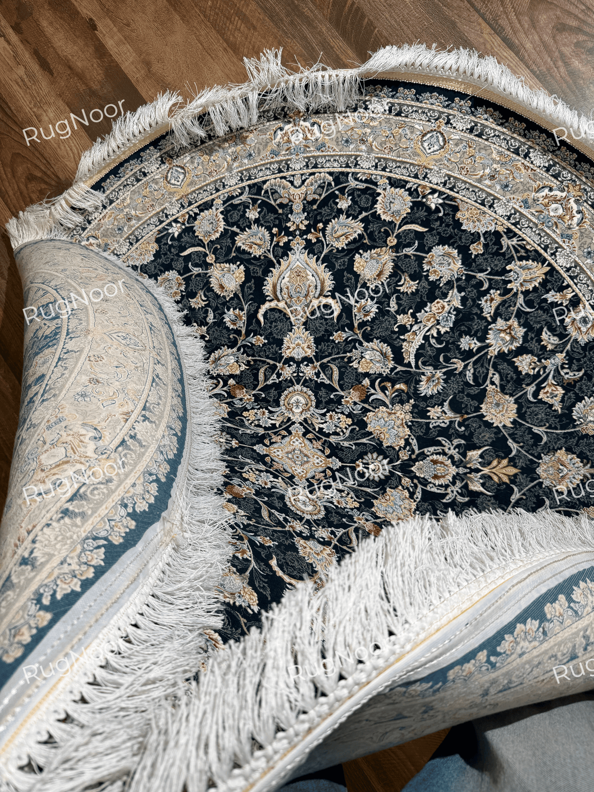 Angled view of the folded Fawaniya rug with traditional floral motifs in ivory, gold, rust, and dusty blue.