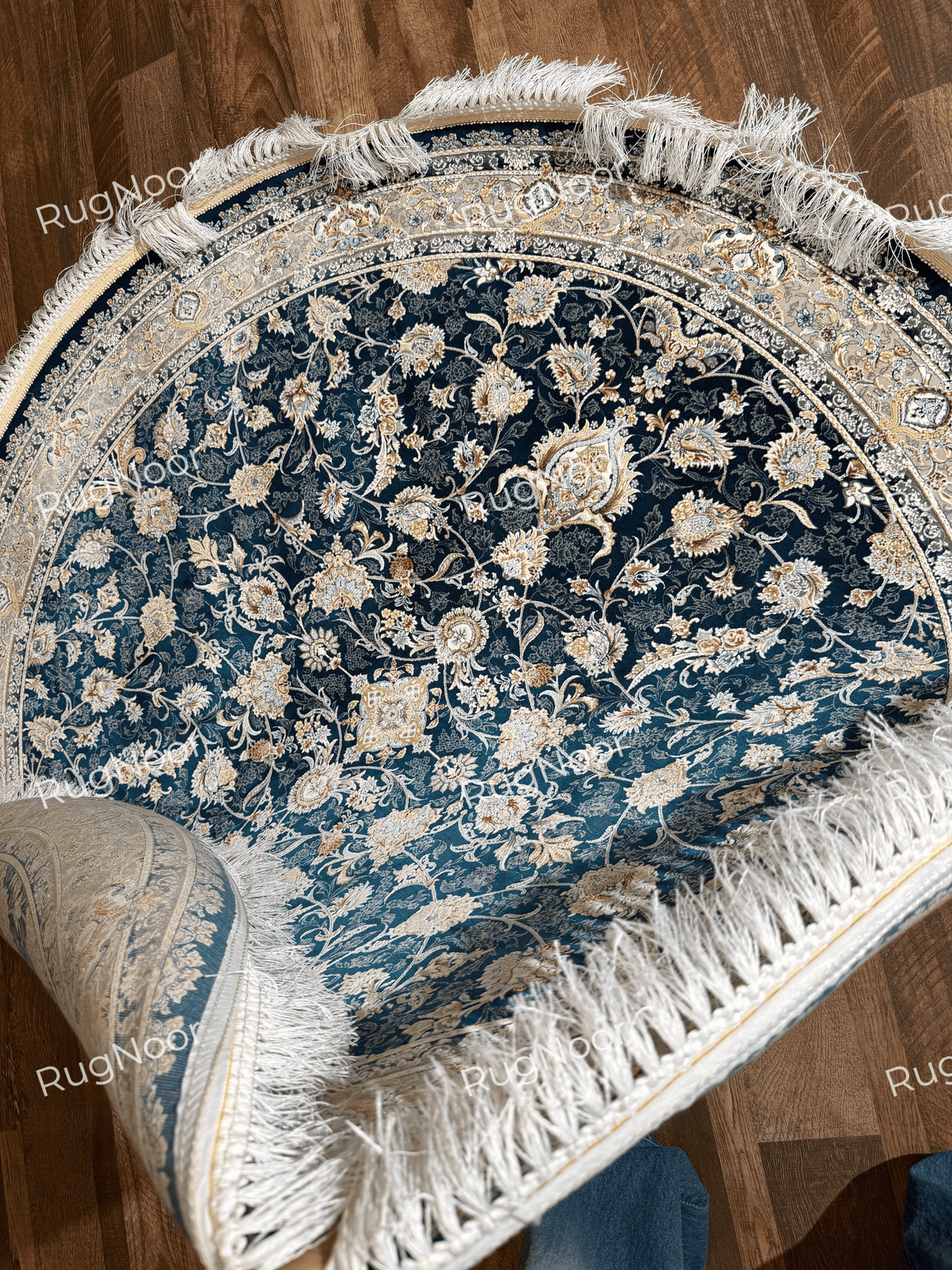 Folded Fawaniya rug displaying the patterned surface, ornate edge, and ivory fringe.