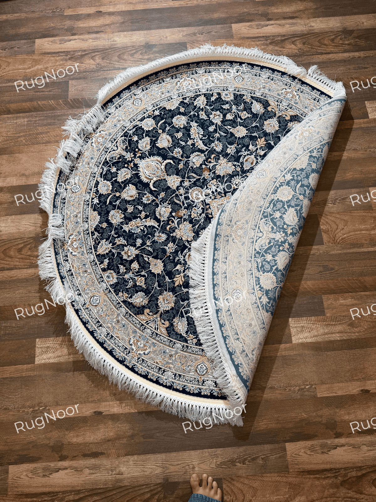 Folded view of the Fawaniya round rug highlighting its navy floral pattern and decorative border.