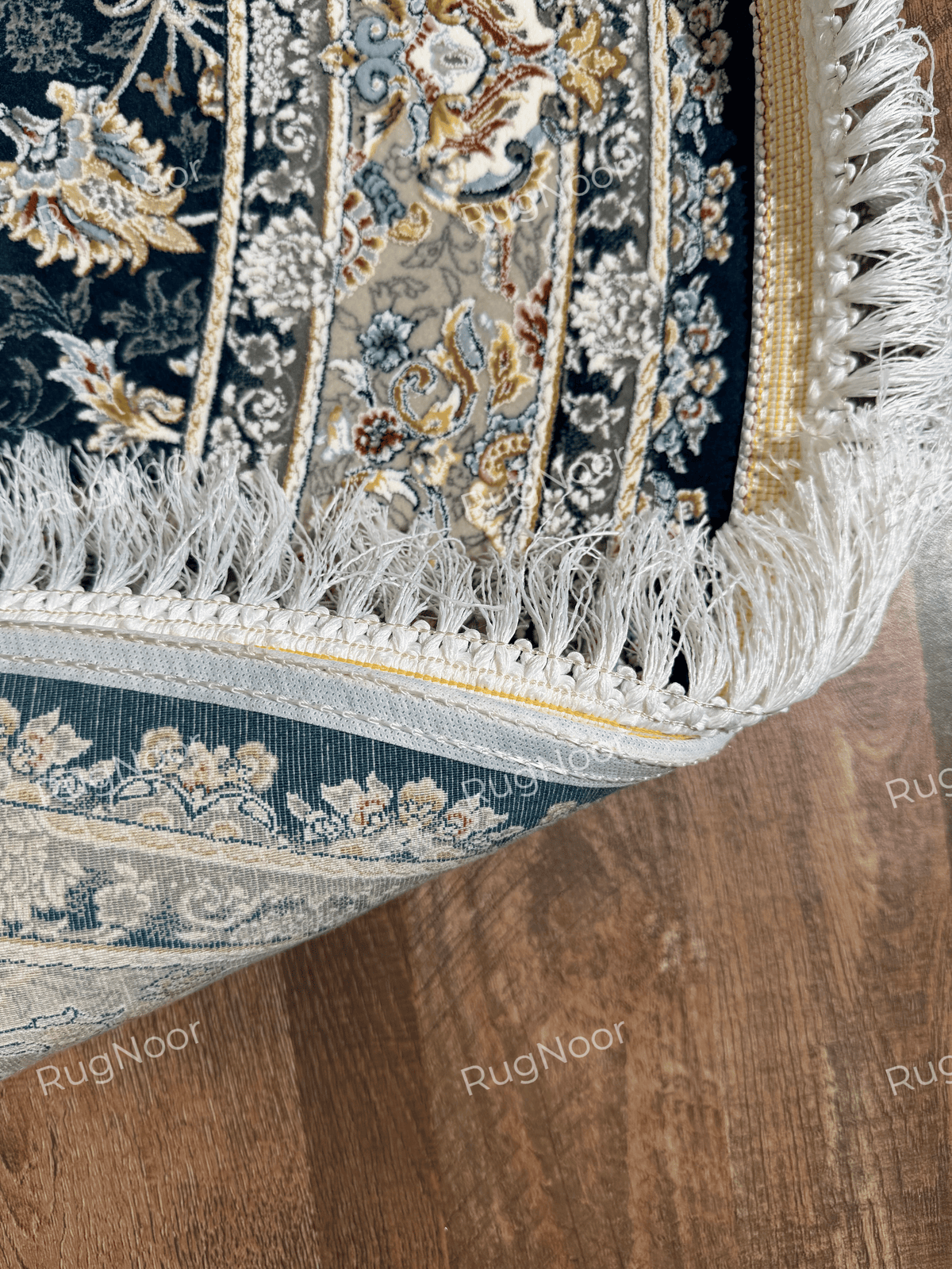 Close-up of the Fawaniya rug's ivory fringe and finished edge beside the navy patterned surface.