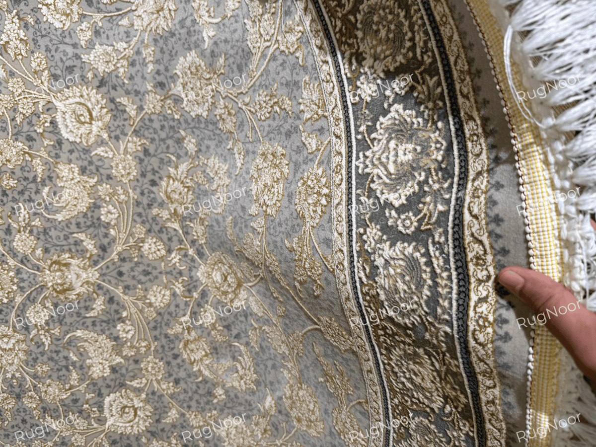 Close-up of the Golnaré grey floral carpet showing ivory fringe, a dark ornamental border, and delicate ivory and gold floral detailing.