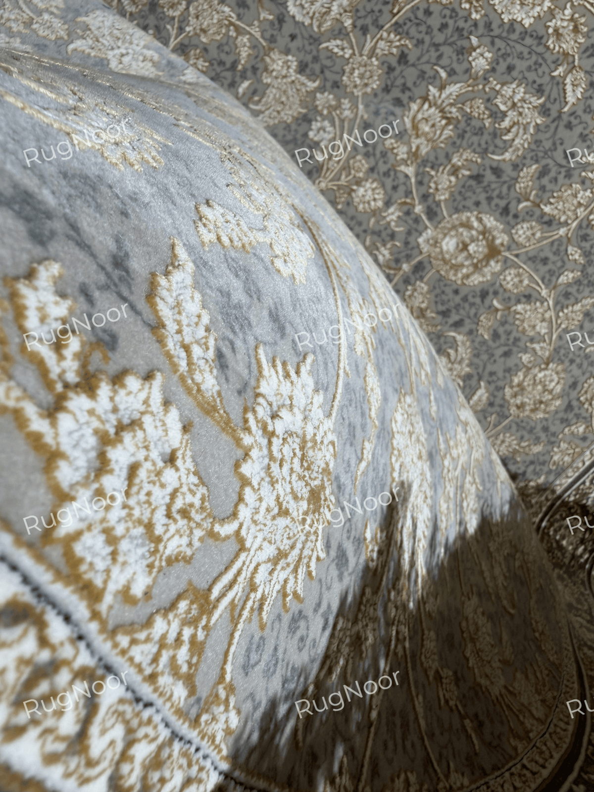 Golnaré round grey carpet folded back to reveal its floral surface, ornamental border, and ivory fringe.