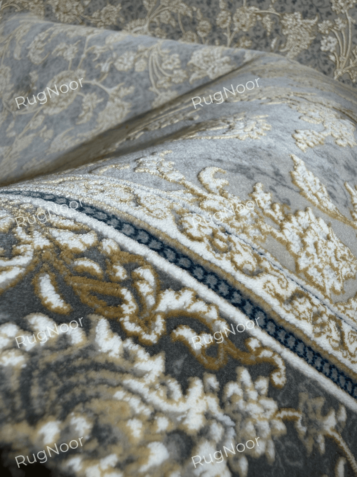 Close-up of the Golnaré carpet's curved grey surface with raised ivory and gold floral motifs and fine decorative outlines.