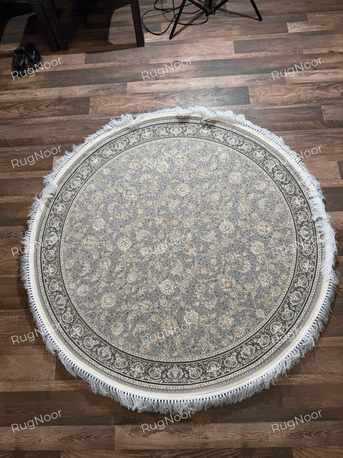 Golnaré round grey floral carpet displayed on a wooden floor, showing the complete floral design, decorative circular border, and ivory fringe.