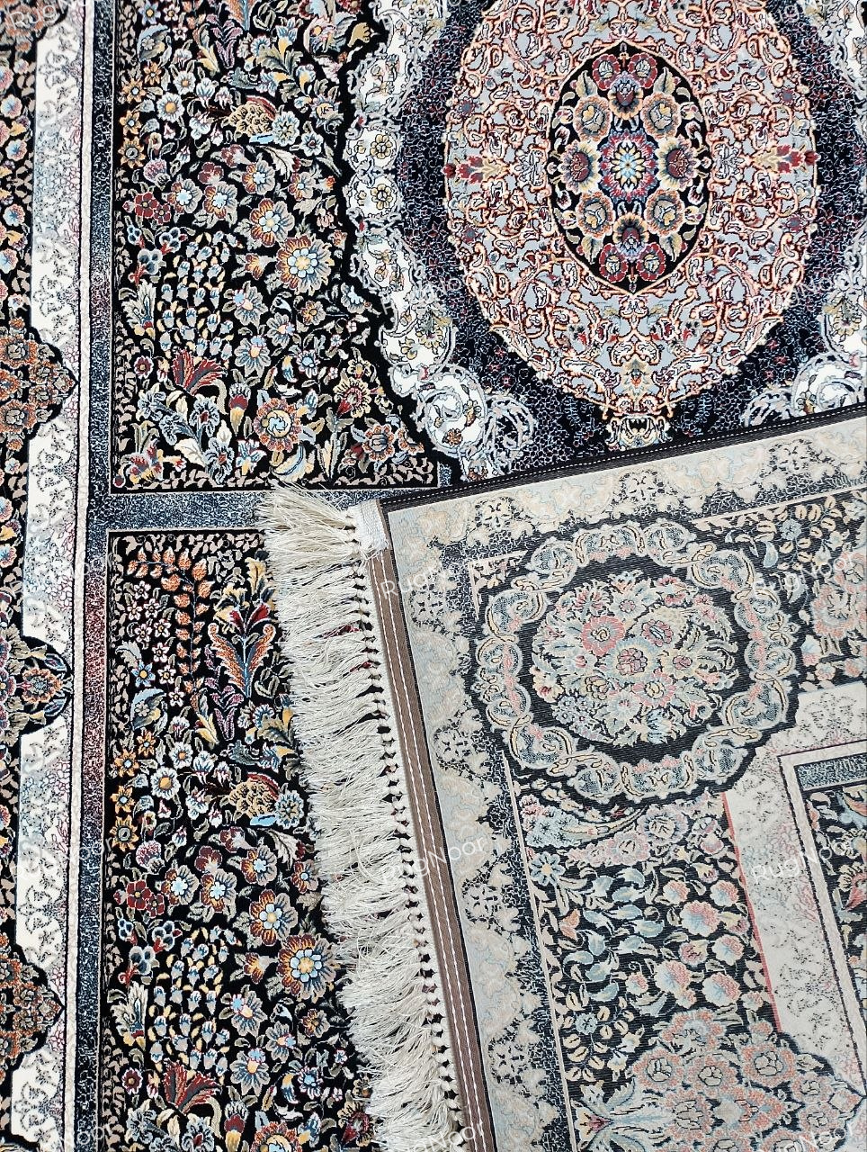Folded Shabrang carpet showing the reverse, dark edge finish, ivory fringe, and patterned front surface.