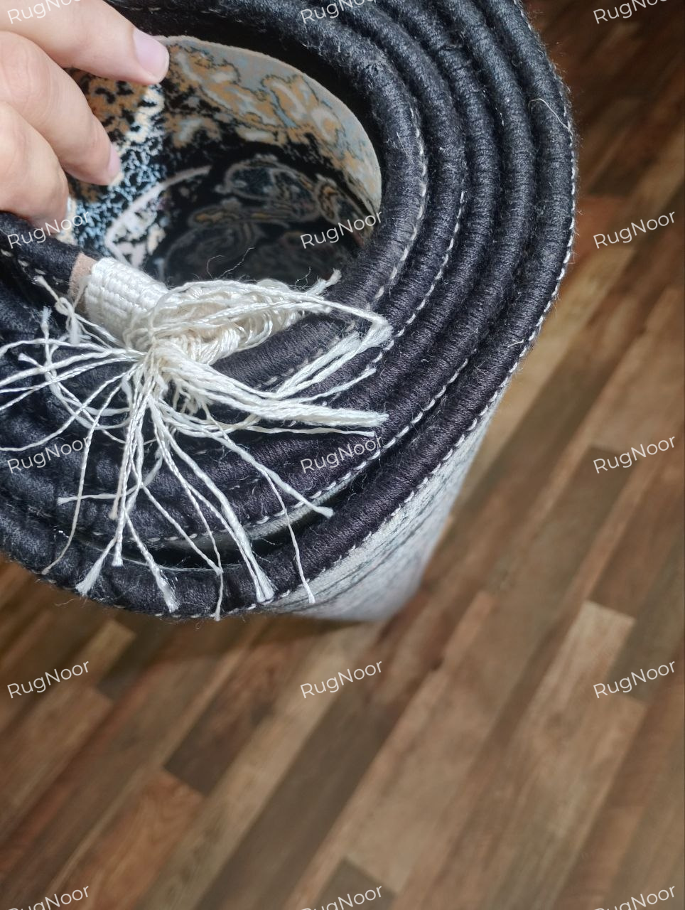 Shabrang traditional floral carpet rolled to show its dark reverse, finished edge, and ivory fringe.