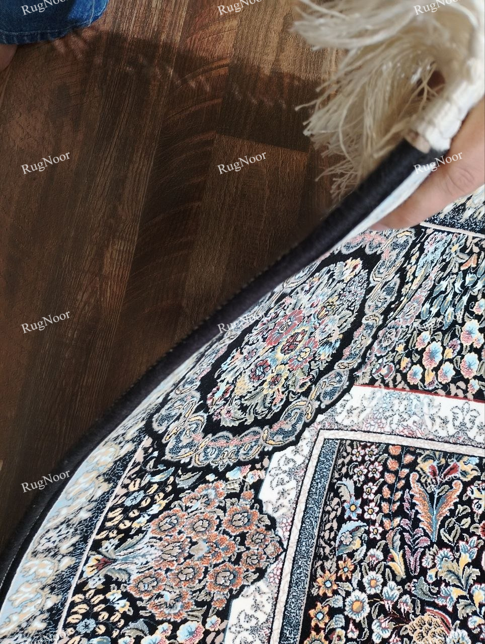 Close-up of the Shabrang traditional floral carpet showing intricate ivory, pale blue, blush pink, and muted gold motifs against a deep black ground.