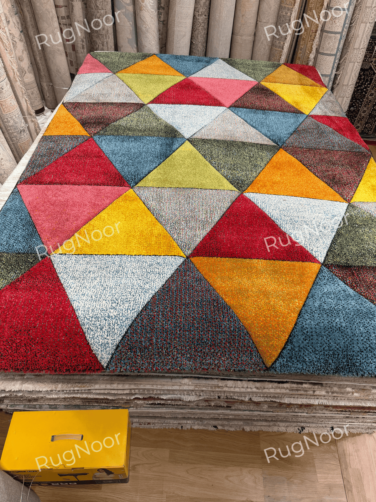 Angled full view of the Prismland colorful geometric carpet with red, orange, yellow, pink, teal, ivory, and olive triangular shapes.