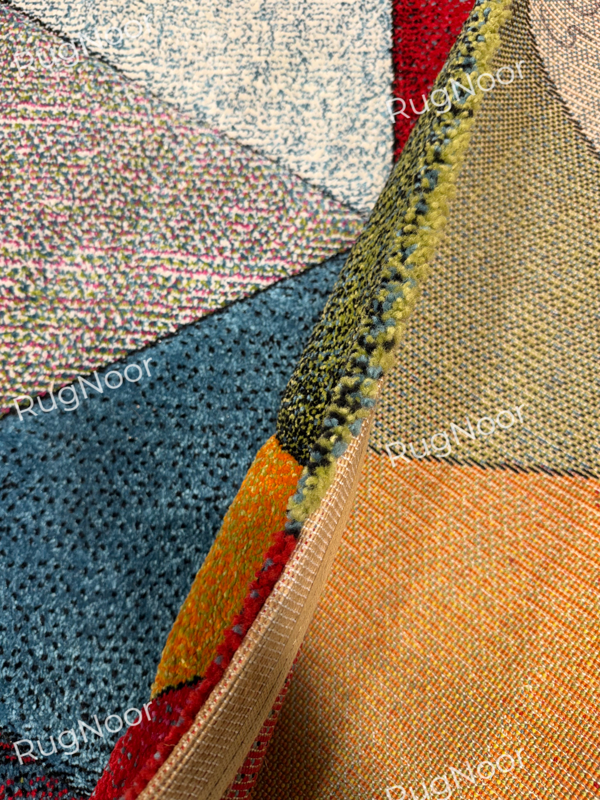 Folded side of the Prismland carpet showing the beige backing, edge binding, and colourful geometric pile.
