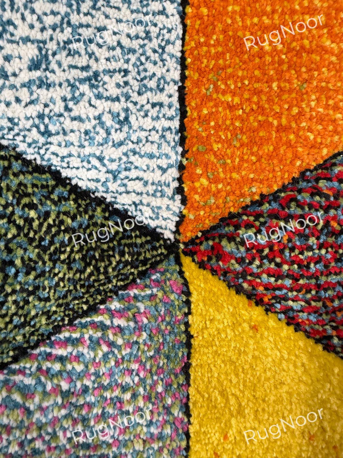 Close-up of the Prismland carpet’s textured pile and the meeting edges of ivory, orange, olive, yellow, and multicoloured geometric sections. 