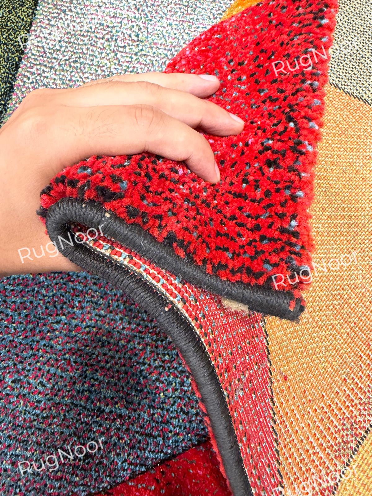 Folded red section of the Prismland carpet showing the pile thickness, dark edging, and backing beneath the colourful surface.