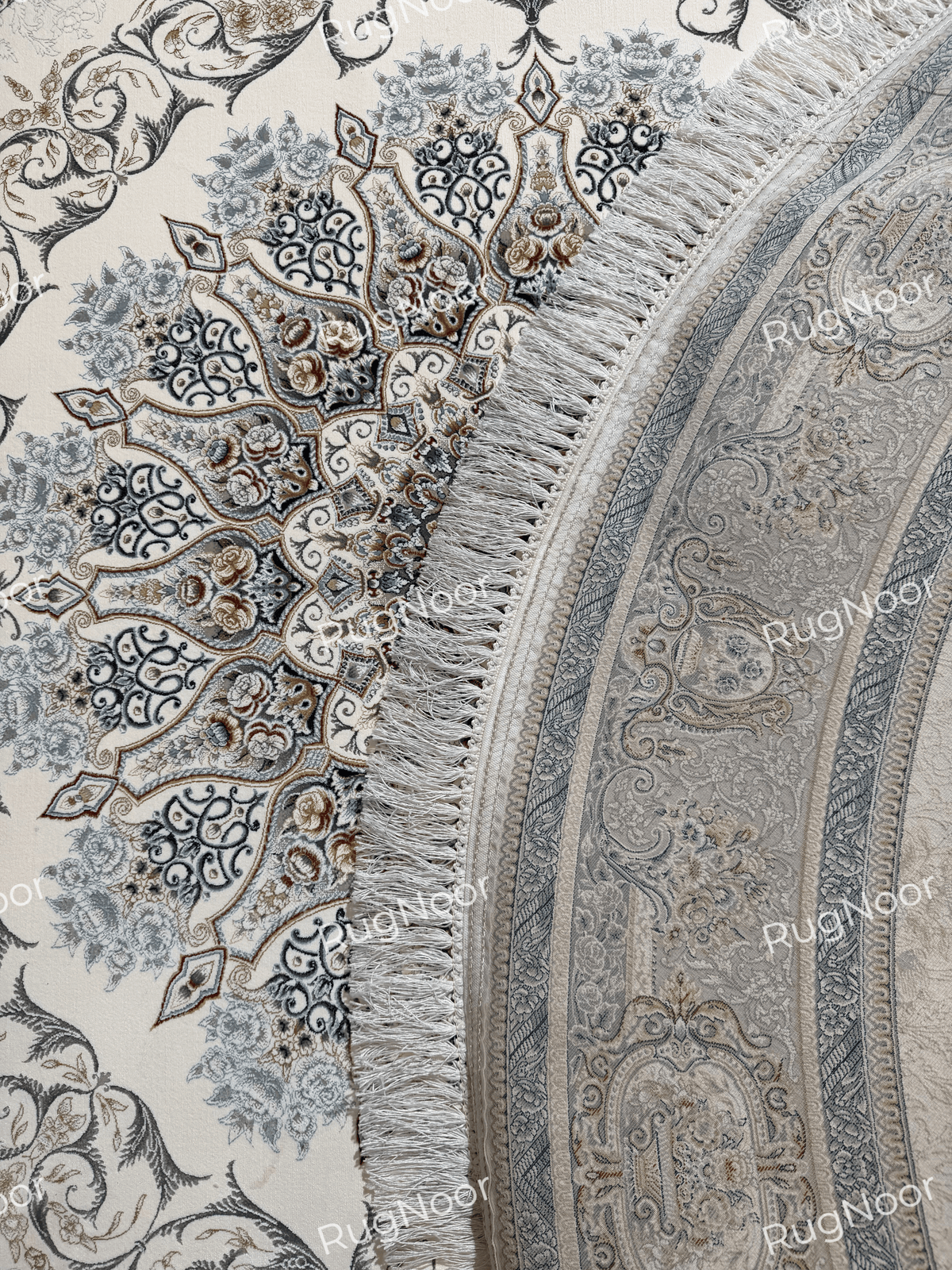 Close view of the Mahzarin carpet’s curved edge, decorative border, ivory fringe, and backside as the rug is lifted.