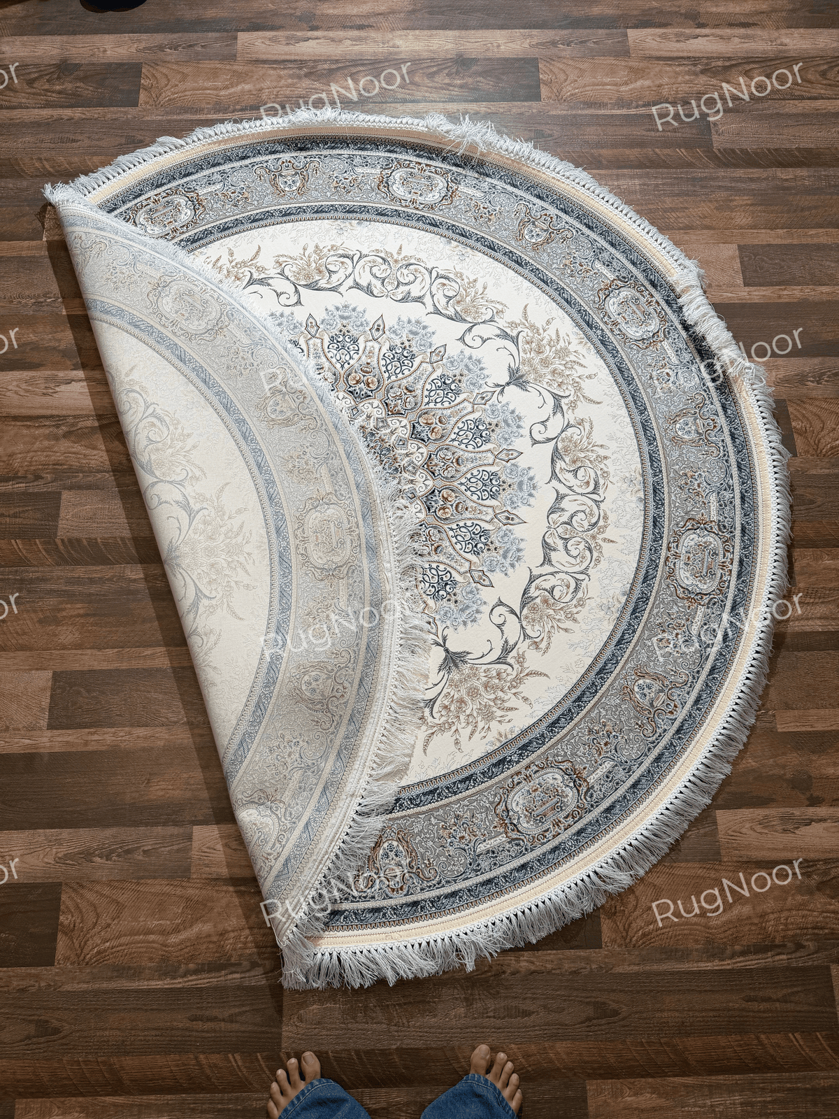 Mahzarin round carpet folded back to show part of the ivory field, intricate central medallion, layered ornamental border, and ivory fringe.
