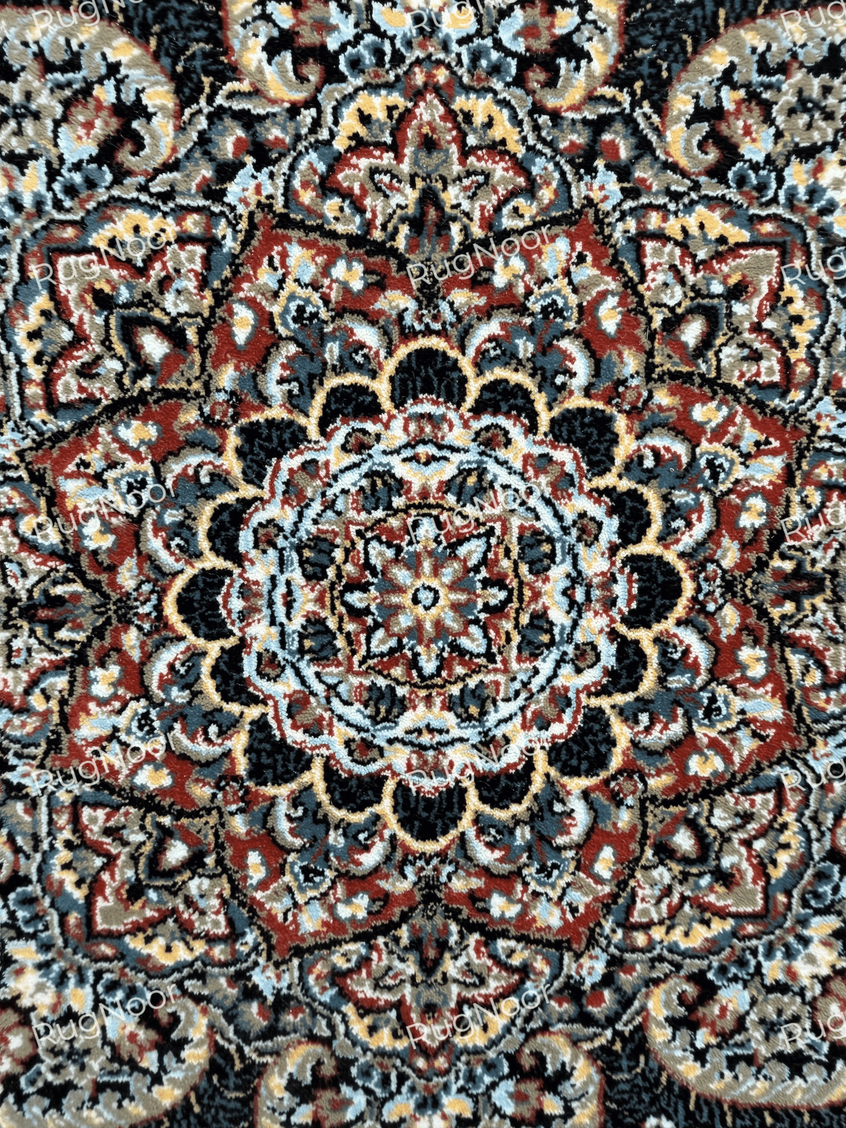 Close-up of the Ravzaran carpet's central floral medallion, featuring symmetrical rust-red, ivory, dusty blue, and gold-accented motifs against a dark background.