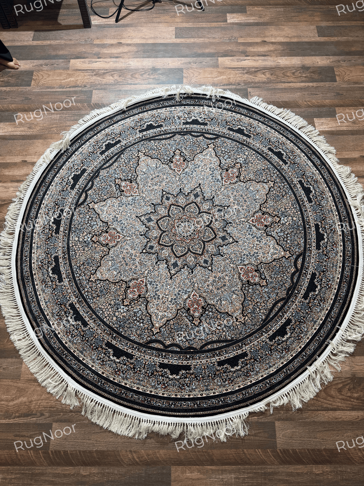 Full view of the Ravzaran round carpet with a prominent floral medallion, dense multicoloured motifs, dark borders, and ivory fringe.