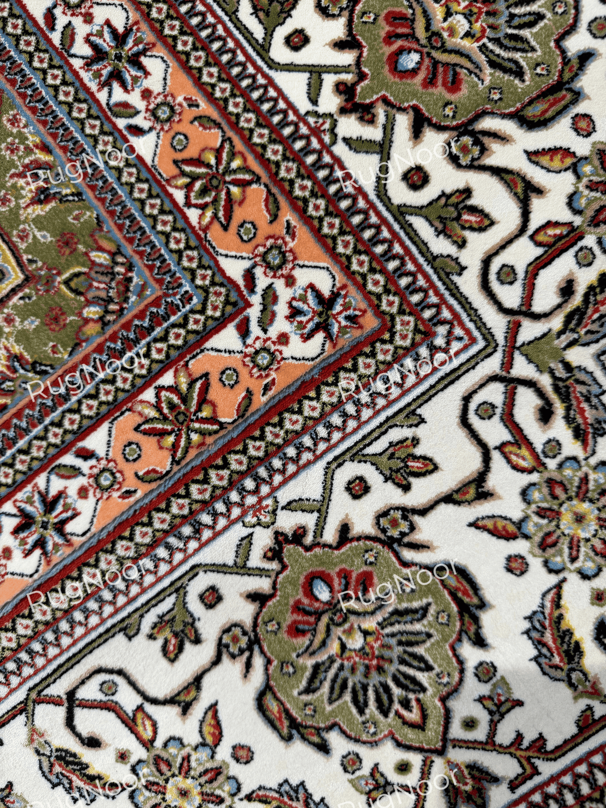 Close-up of the Anbara carpet's ivory border with olive floral motifs and layered coral, dark blue, and cream geometric edging.
